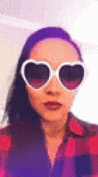 a woman wearing a plaid shirt and heart shaped sunglasses is taking a selfie .