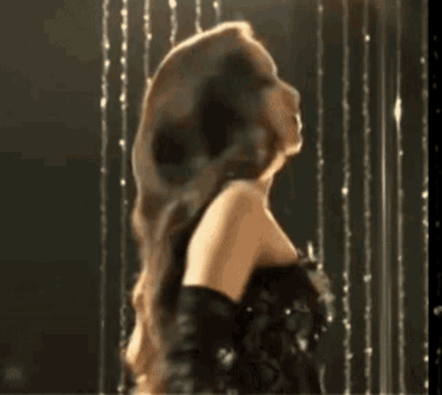 a woman in a black dress and black gloves is dancing in front of a waterfall