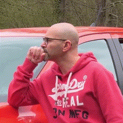 a bald man wearing a red hoodie that says superdry real on it