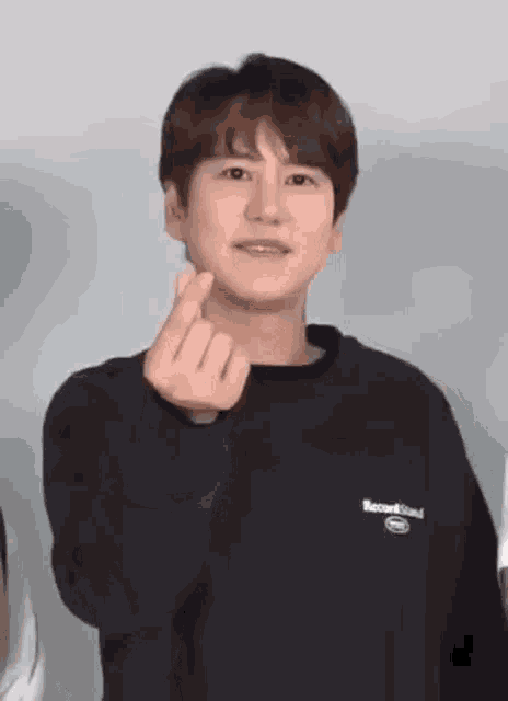a young man in a black sweatshirt is making a heart shape with his fingers .