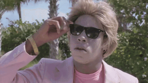 a man wearing a pink suit and sunglasses is looking at the camera .