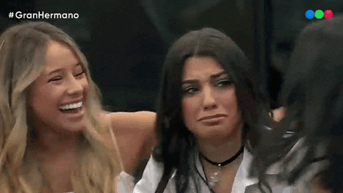 two women are laughing and one is making a face in front of a sign that says gran hermano