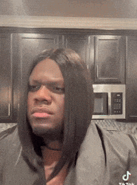 a man wearing a wig is standing in a kitchen with a microwave behind him