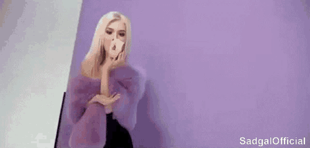 a woman in a purple fur coat is blowing a kiss while holding a donut .