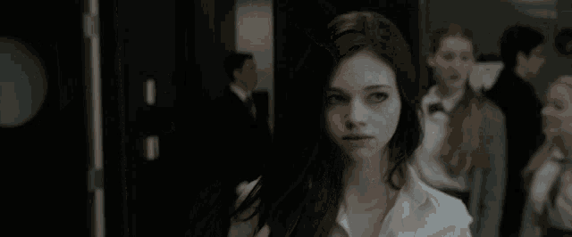 a woman in a white shirt looks at the camera with another woman in the background