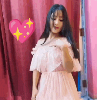 a woman in a white dress is standing in front of a pink curtain with a heart in the background .
