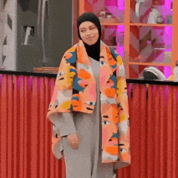 a woman wearing a hijab and a colorful scarf is standing in front of a kitchen counter .