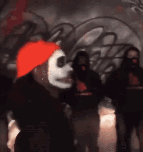 a man wearing a white mask and an orange hat is standing in front of a wall with graffiti .