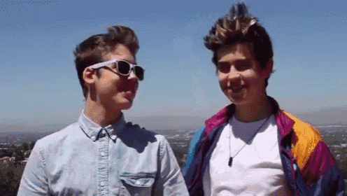 two young men wearing sunglasses are standing next to each other and looking at each other