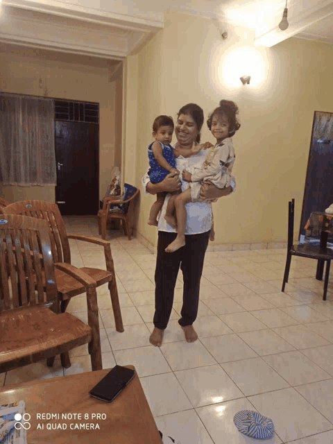a woman holding two children in a living room with a redmi note 8 pro