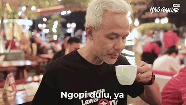 a man drinking a cup of coffee with the words ngopi dulu ya written on his shirt