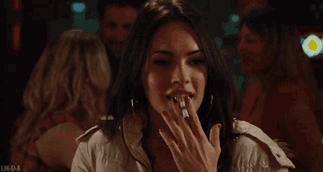 a woman is smoking a cigarette in a crowded bar .