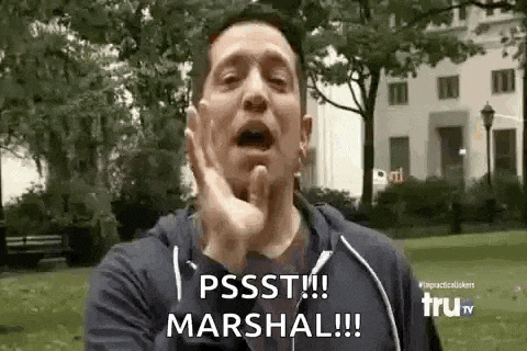 a man is making a funny face and saying pssst !!! marshal !!! in a park .