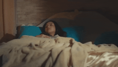 a woman is laying in a bed with a blue pillow .
