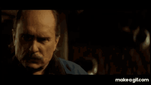 a man with a mustache is looking at the camera in a dark room .