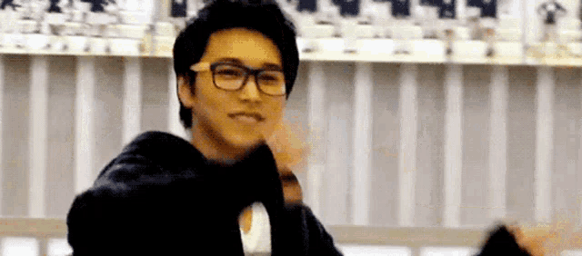 a young man wearing glasses and a black jacket is standing in front of a striped wall .