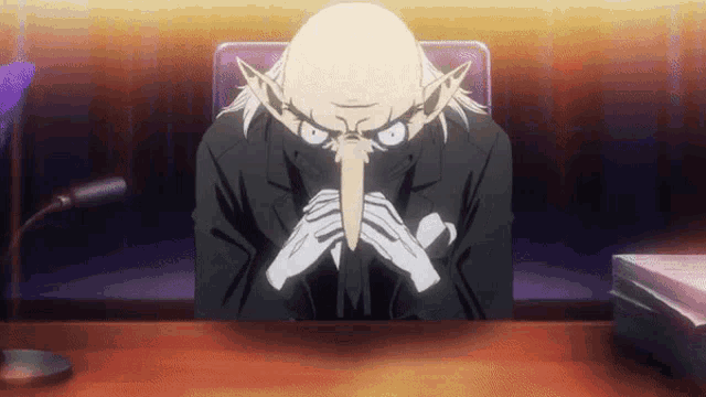 a man in a suit is sitting at a desk with his hands folded