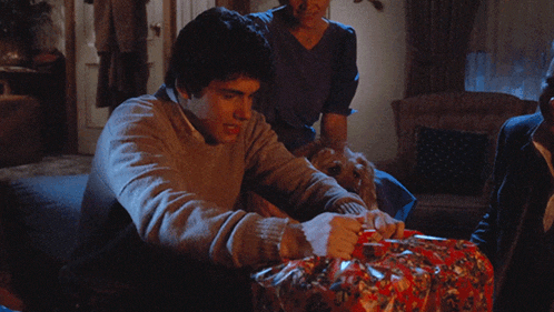 a man sitting on a couch with a dog looking at a gift