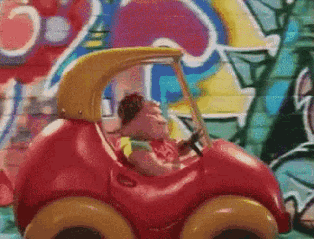 a red toy car with a yellow top is parked in front of a wall with graffiti .