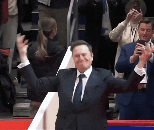 a man in a suit and tie is applauding with his arms outstretched