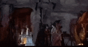 a group of people are standing around a table in a dark room with a statue in the background .