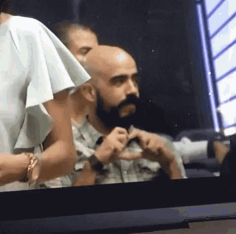a bald man with a beard is making a heart with his hands