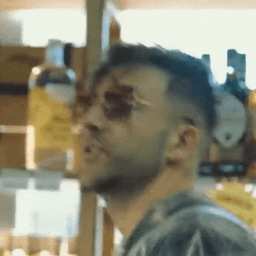 a man wearing sunglasses is standing in front of a shelf with bottles on it