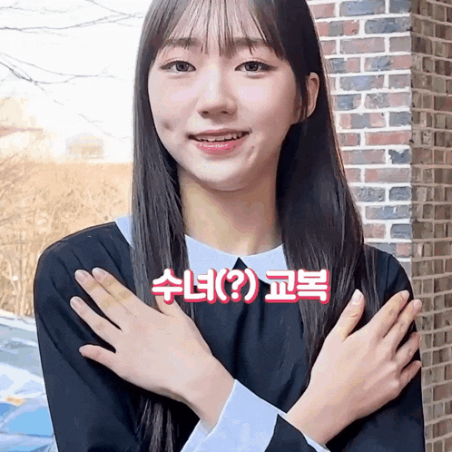 a girl in a school uniform holds her hands up in front of a brick building
