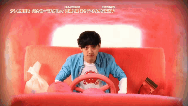 a man in a blue shirt is sitting in a car with a red steering wheel