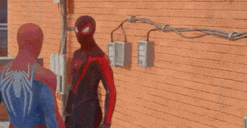 two spidermans are standing next to each other on a sidewalk .