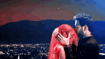 a man kisses a woman with red hair in front of a city at night