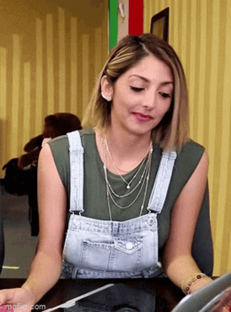 a woman in overalls is sitting at a table