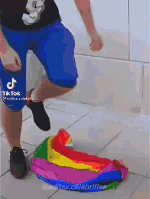 a man in blue shorts is standing next to a rainbow flag on the ground .