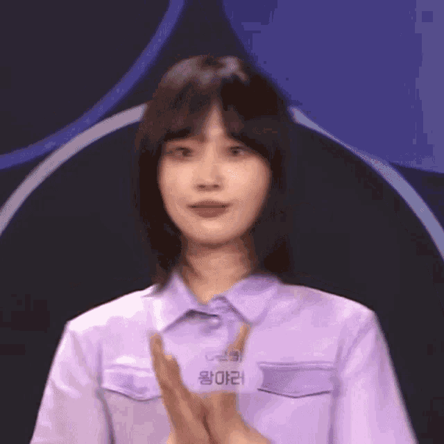a woman in a purple shirt is clapping her hands in front of a dark background .