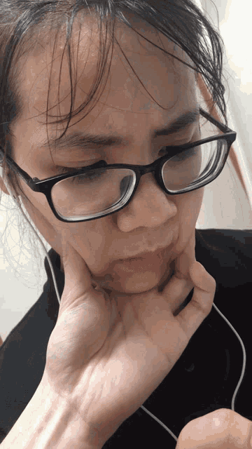 a woman wearing glasses and earbuds holds her chin