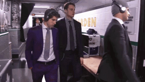 three men in suits are walking in a hallway with the word garden on the wall behind them