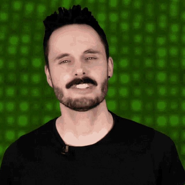 a man with a beard and mustache is smiling in front of a green background .