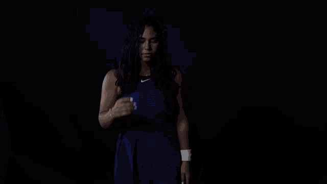 a woman wearing a blue nike tank top is standing in the dark