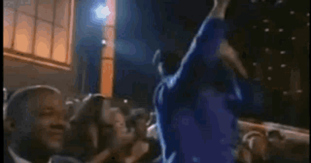 a man in a blue jacket is dancing in front of a crowd .