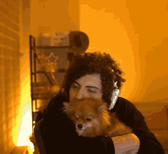 a man wearing headphones is holding a small dog in his arms