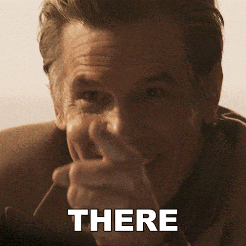 a man in a suit is pointing at the camera with the word there above him