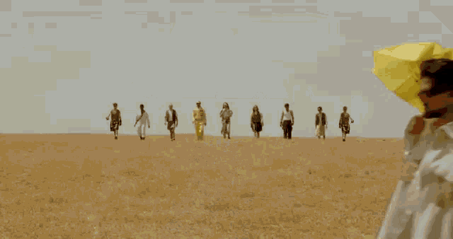 a group of people are walking in a field while a woman holds a yellow umbrella .