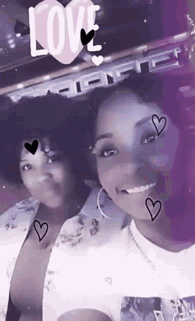 two women are posing for a picture with a pink heart that says love on it