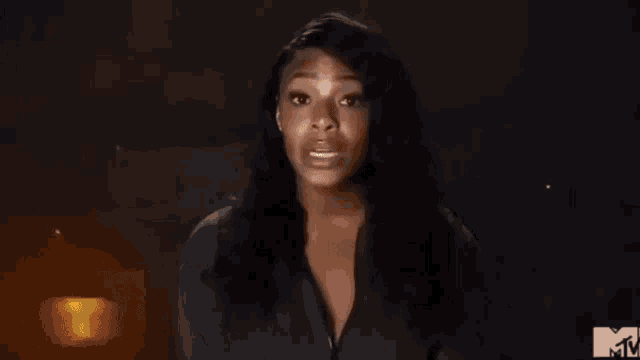 a woman is standing in front of a fire in a dark room and making a funny face .