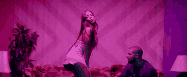 a man and a woman are dancing on a couch in a living room with purple lights .