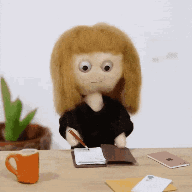 a doll sits at a desk with a notebook and a pen