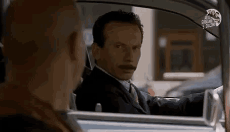 a man in a suit and tie is driving a car and looking out the window .