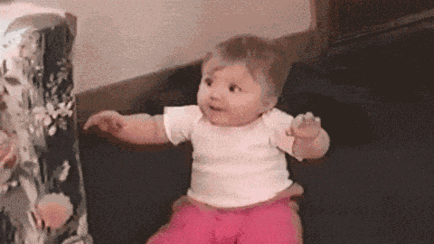 a baby in a white shirt and pink pants is standing in front of a gift box .