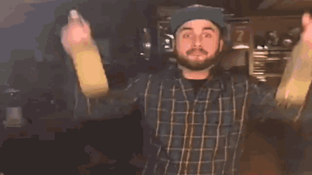 a man in a plaid shirt is holding a bottle of beer in his hand .