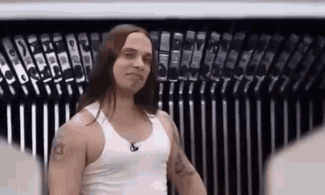 a man with long hair and a tattoo on his arm is standing in front of a row of phones .